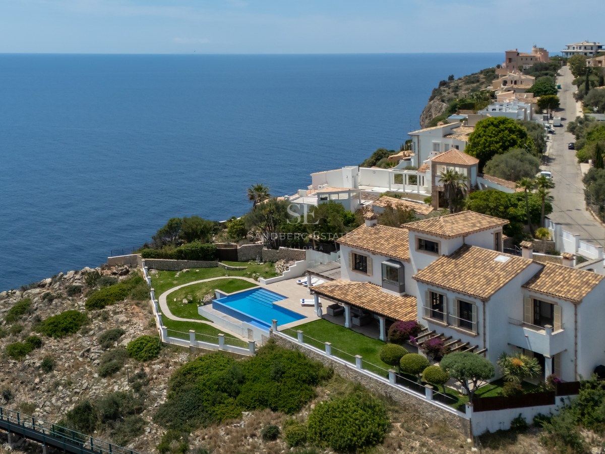 Vue aérienne d'une villa méditerranéenne blanche avec piscine sur une falaise surplombant la mer bleue.