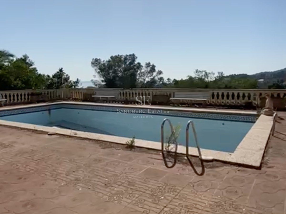 Piscina rectangular exterior con balaustrada de piedra y vistas lejanas al mar bajo un cielo despejado.
