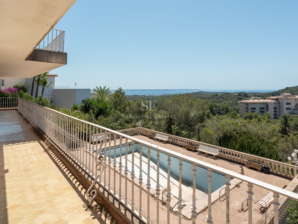 Terraza elevada con barandilla de hierro blanco, vistas a la piscina, pinos y el mar Mediterráneo al fondo.