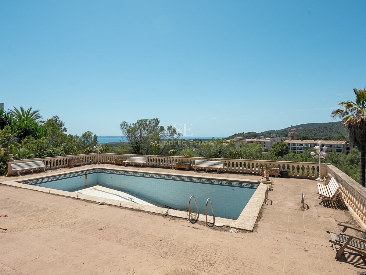 Piscina rectangular vacía en una terraza de terracota con balaustradas de piedra y vistas lejanas al mar.