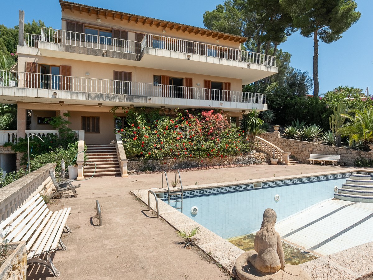 Villa mediterránea de varios niveles con amplias terrazas y una gran piscina vacía rodeada de vegetación exuberante.