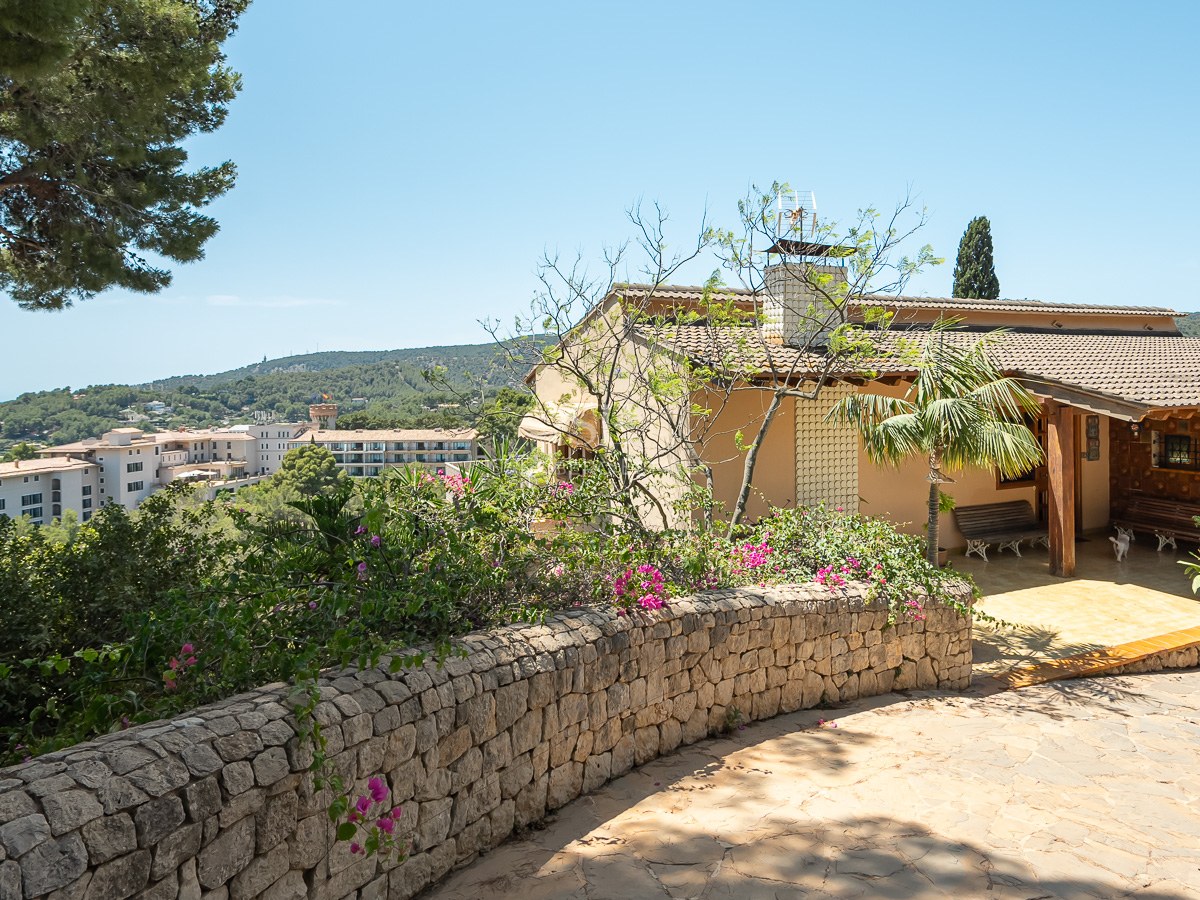 Villa tradicional mediterránea con muro de piedra y porche con vistas a las colinas y el mar al fondo.