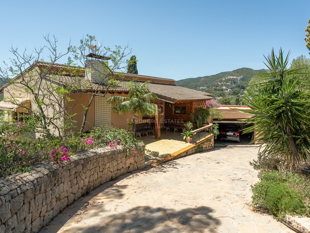 Villa tradicional mediterránea con entrada de piedra, tejado de terracota y garaje rodeada de vegetación exuberante.