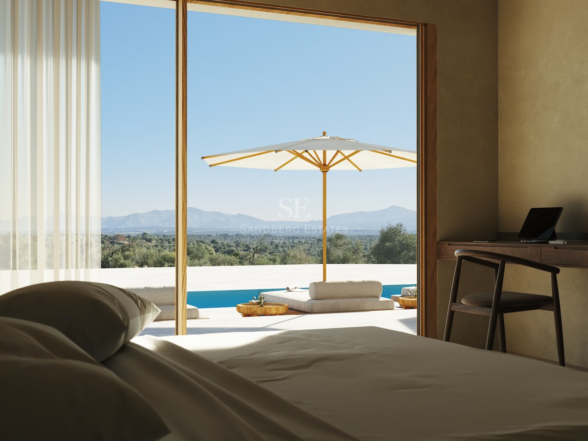Schlafzimmer mit Holzschreibtisch und großen Glastüren, die auf eine Terrasse mit Pool und Bergblick führen.