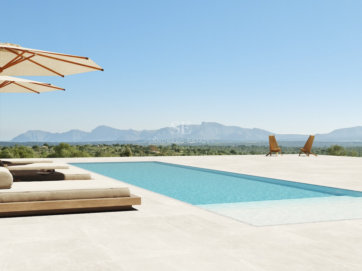 Rechteckiger Pool umgeben von hellen Steinfliesen, luxuriösen Tagesbetten und Sonnenschirmen vor einer Bergkulisse.