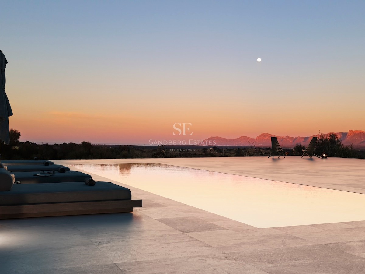 Ein Infinity-Pool und eine Steinterrasse in der Dämmerung mit Blick auf eine Gebirgskette bei Sonnenuntergang.