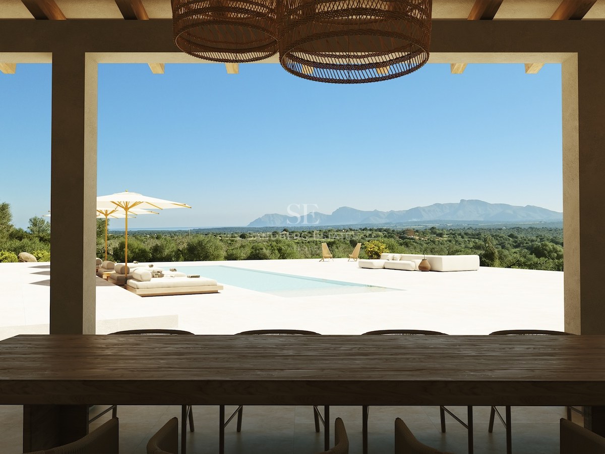 Schattige Terrasse mit dunklem Holztisch und Blick auf einen Pool und eine Bergkette unter blauem Himmel.