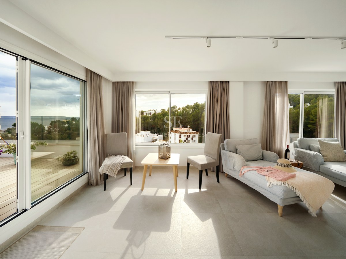 Salón contemporáneo lleno de luz natural con grandes ventanales y acceso a terraza con vistas al mar.