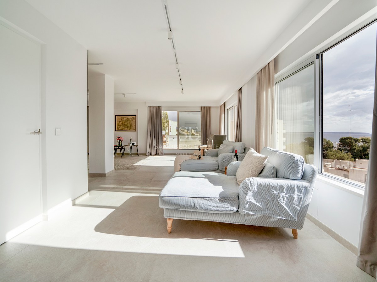 Salón moderno con sofás a rayas azul claro y grandes ventanales con vistas al mar y la costa mediterránea.