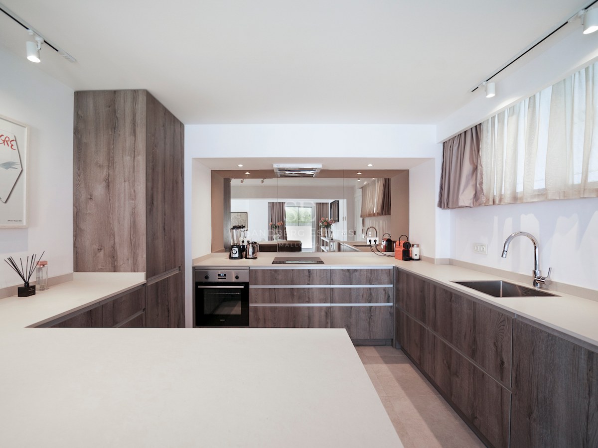 Cocina minimalista con armarios de madera oscura, encimeras blancas y rieles de iluminación modernos.