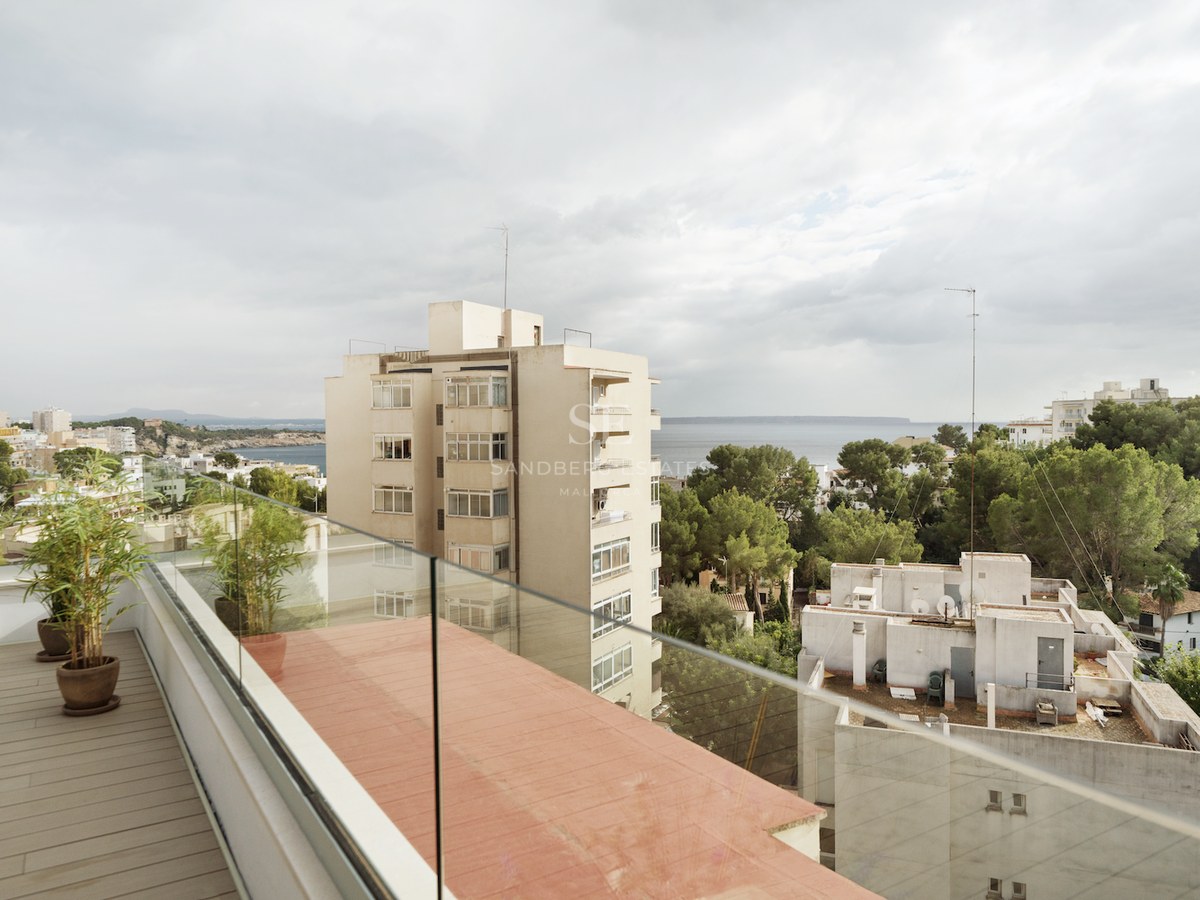 Terraza contemporánea con suelo de madera y barandillas de cristal con vistas a la ciudad y al mar Mediterráneo.