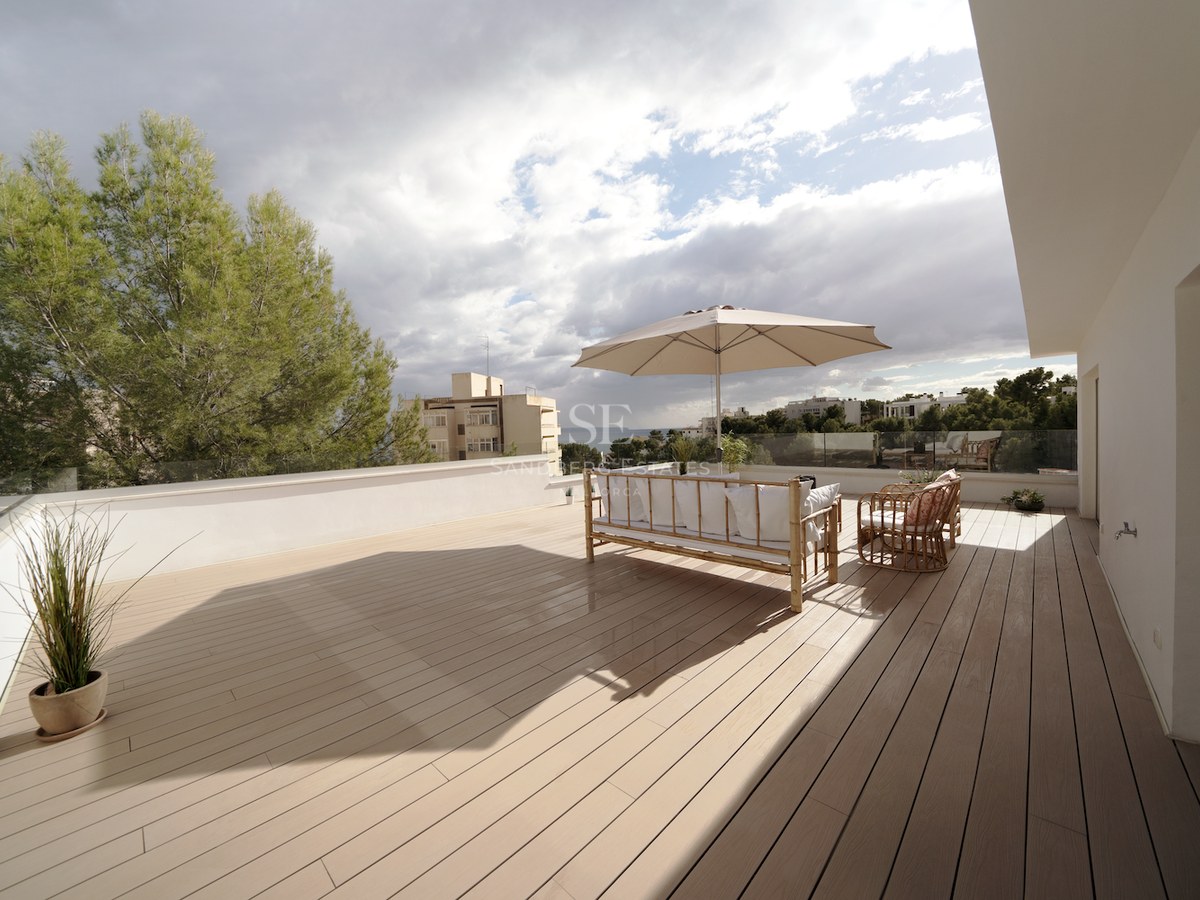 Terraza espaciosa con suelo de tarima, muebles de bambú, sombrilla beige y barandilla de cristal con vistas al mar.