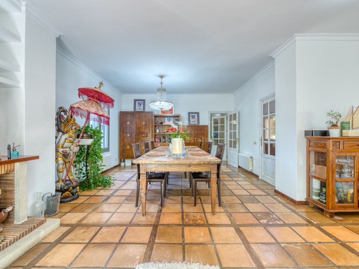 Grande salle à manger avec table en bois, sol en terre cuite, cheminée et statue décorative.