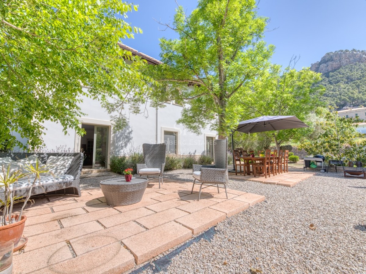 Terrasse ensoleillée avec salon en résine tressée et table à manger sous les arbres, face aux montagnes.