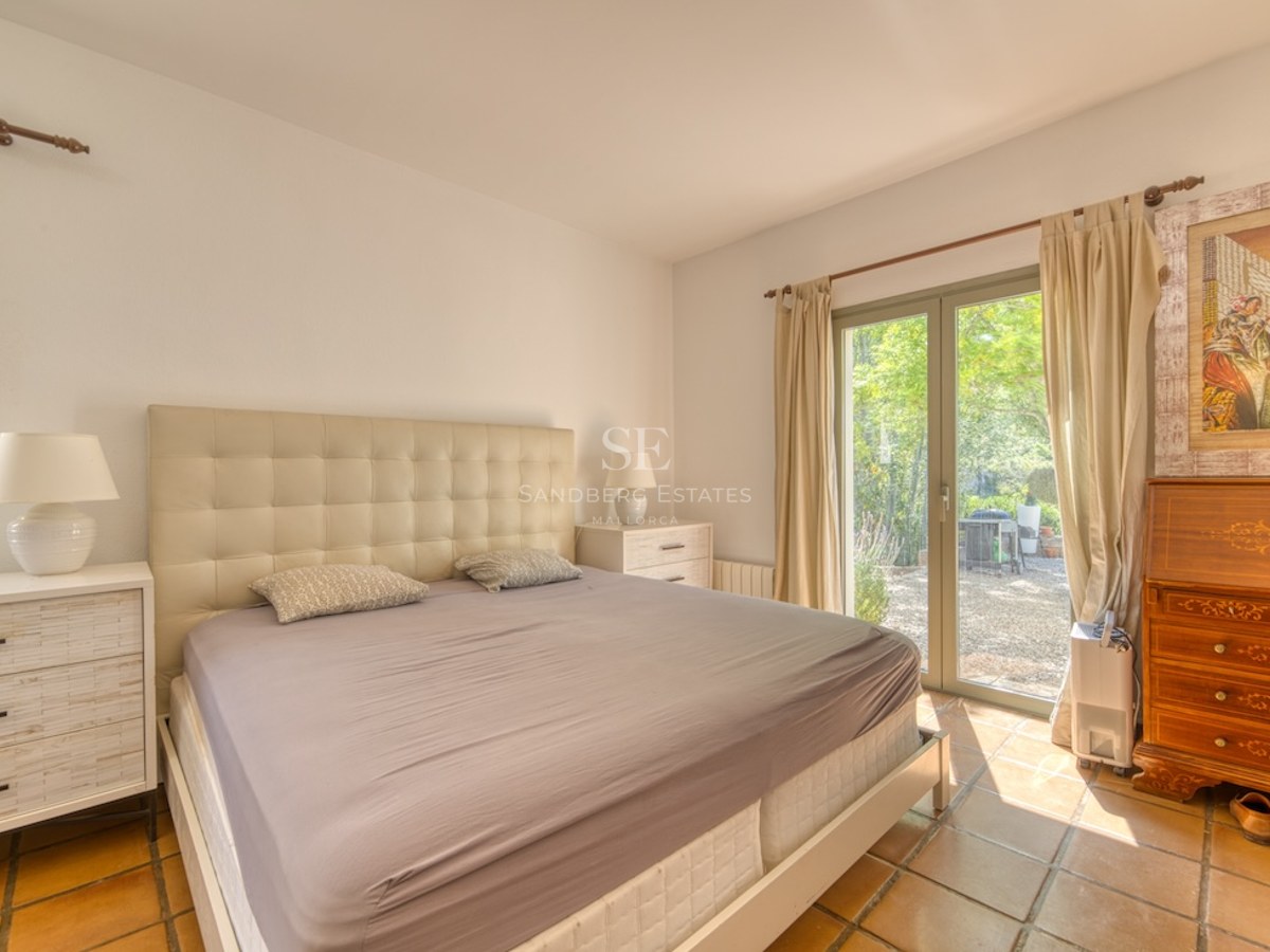 Chambre avec lit double, tête de lit capitonnée, sol en terre cuite et porte vitrée donnant sur le jardin.