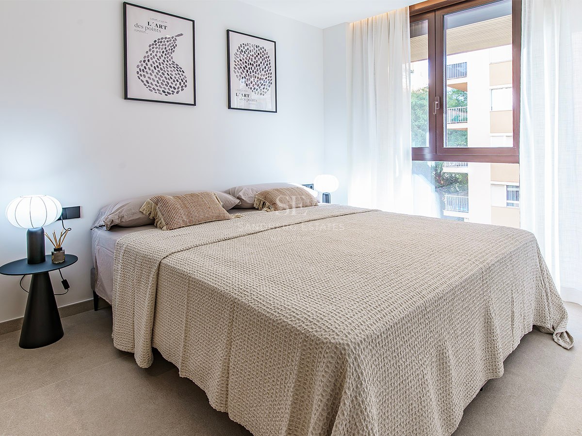 Ljust sovrum med stor säng, beige sängkläder, designerlampor och fönster med skira gardiner.