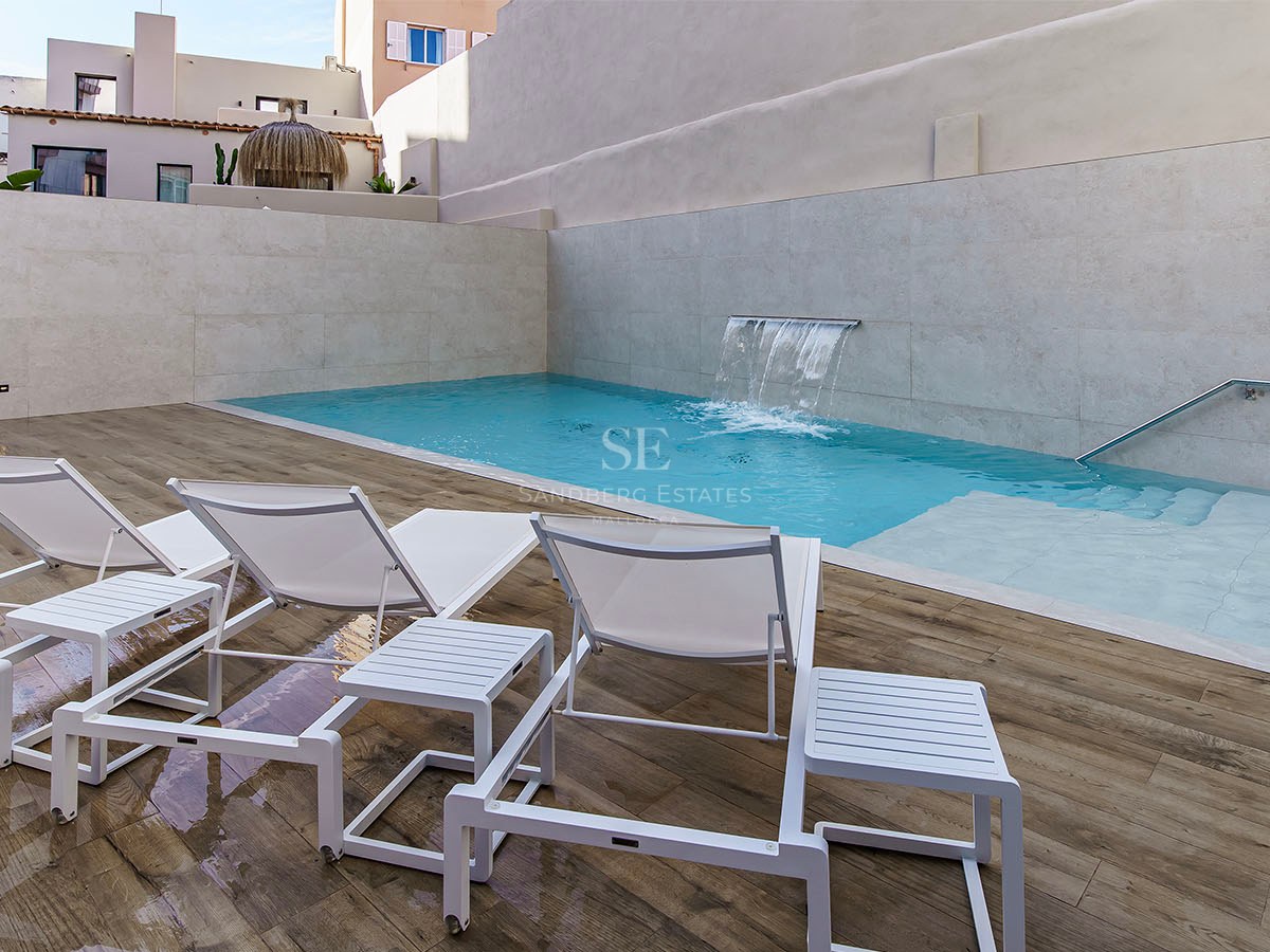 Turkos pool med integrerat vattenfall, vita solstolar på trädäck och stenväggar.
