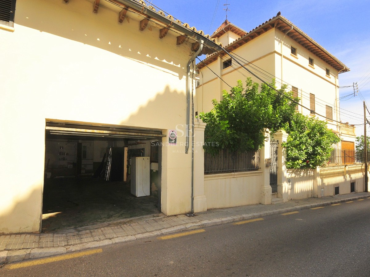 Exteriör av en beige byggnad i traditionell stil med ett öppet garage och tegeltak under en klar himmel.