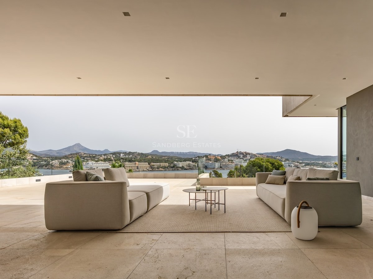 Contemporary covered terrace with neutral-toned sofas and an expansive view of the coastline and mountains.