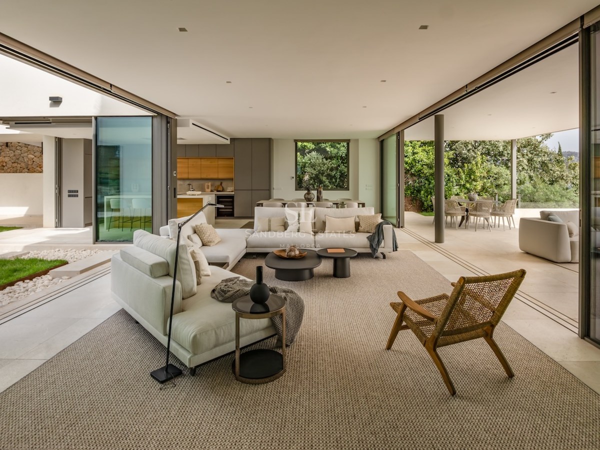 Spacious contemporary living room with cream sofas and glass walls opening onto a terrace and lush garden.