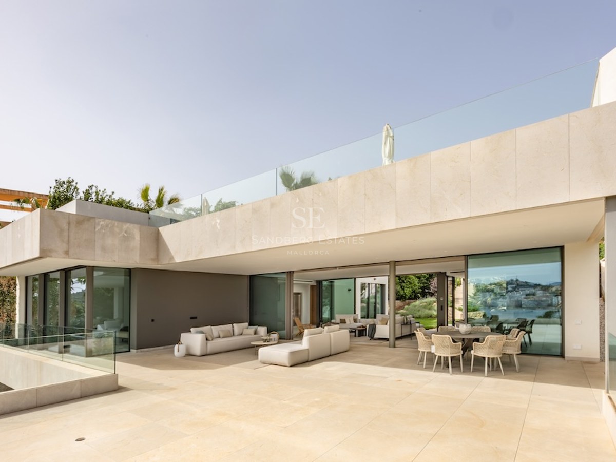 A wide sun-drenched stone terrace with modern lounge seating and a dining area under a large architectural overhang.