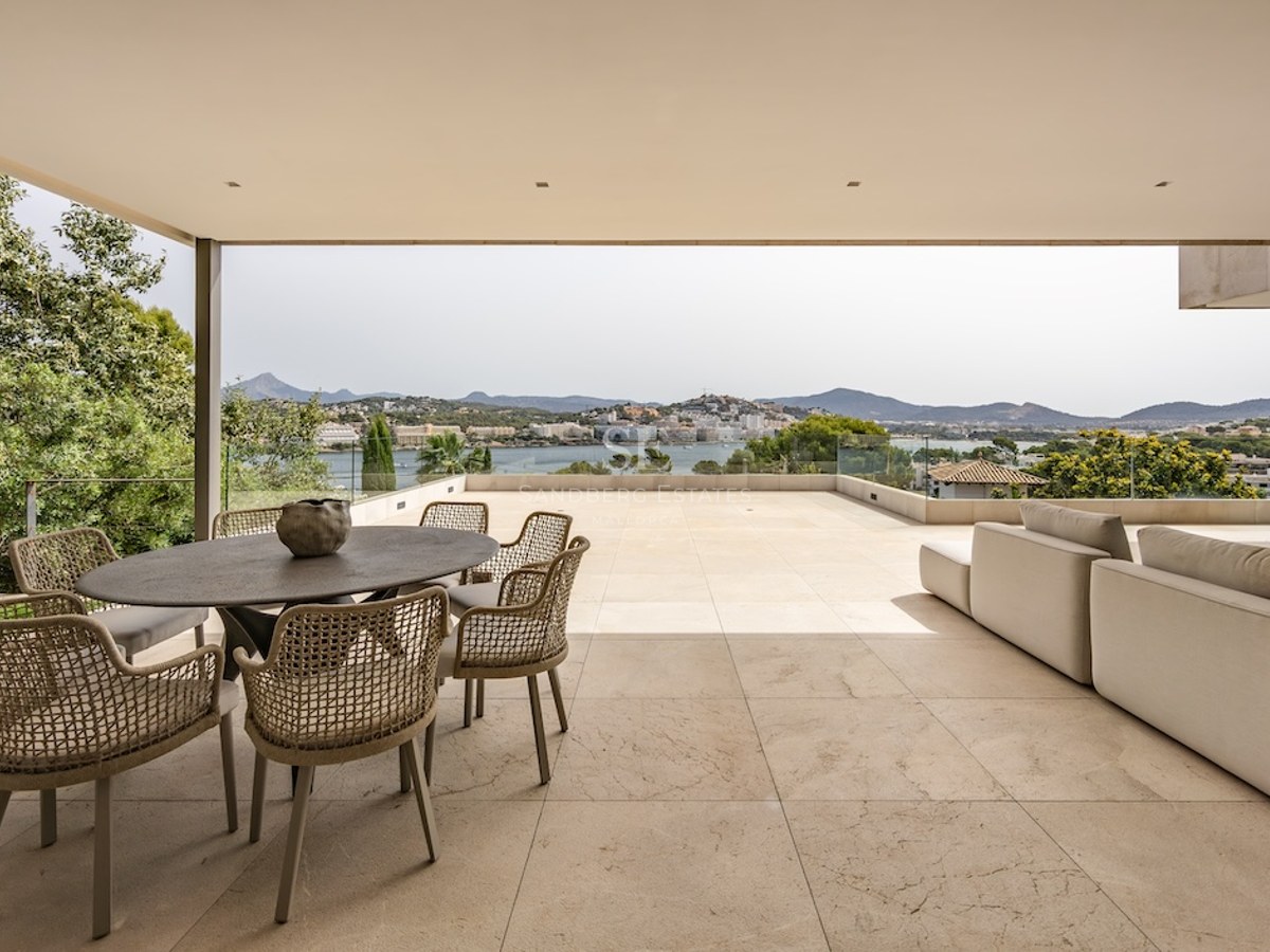 Covered terrace with stone flooring, outdoor dining set, and lounge sofa overlooking a bay and mountains.