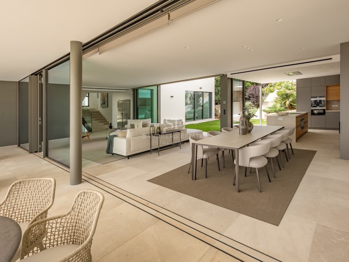 Modern open-plan living and dining room with large sliding glass doors opening to a sunlit garden.