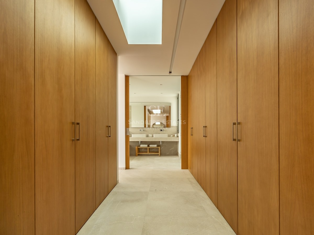 A symmetrical hallway of floor-to-ceiling oak wardrobes lit by a rectangular skylight leading to a bathroom.