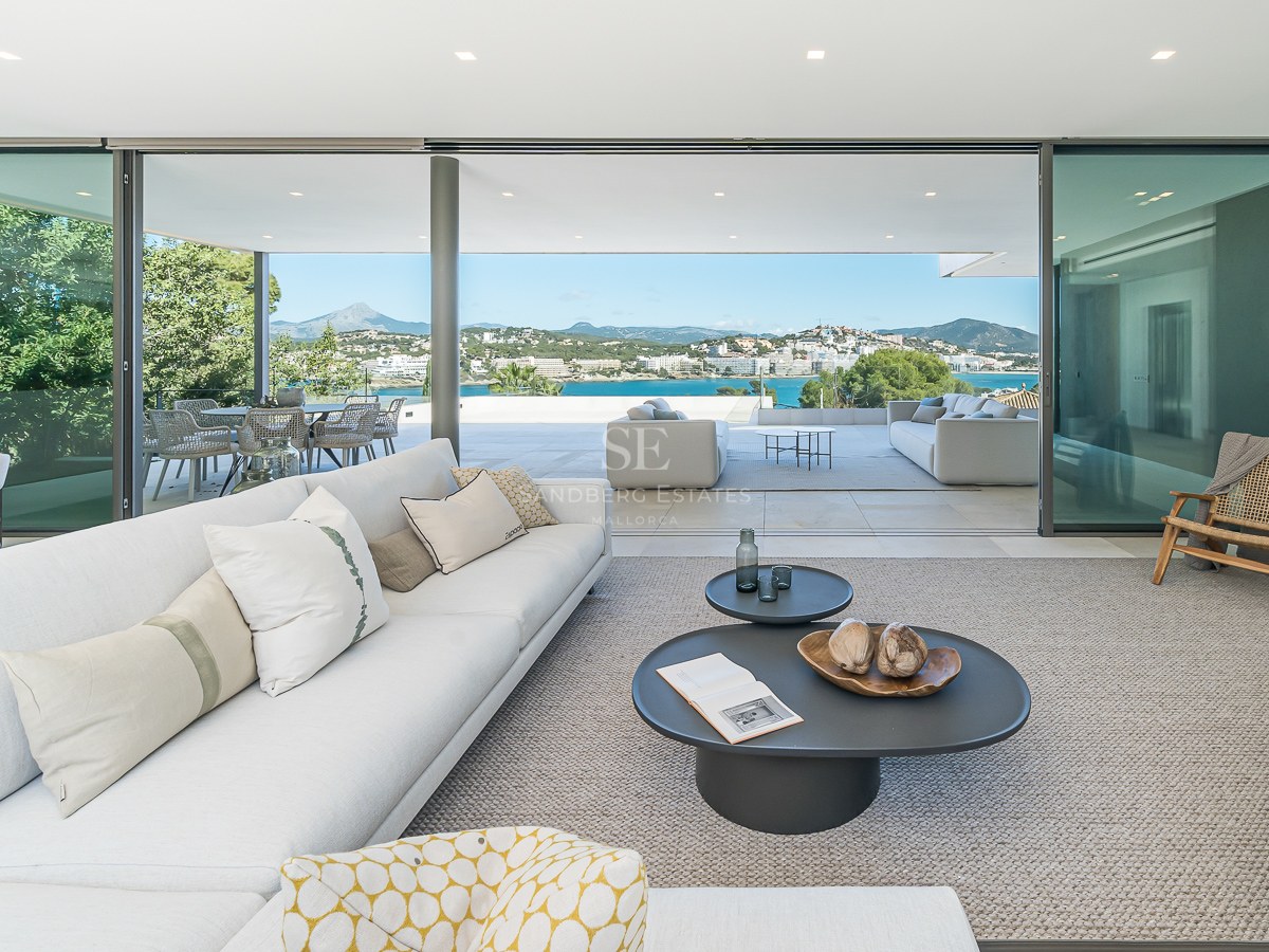 Modernt vitt vardagsrum med glasdörrar och terrass med panoramautsikt över havet och bergen.