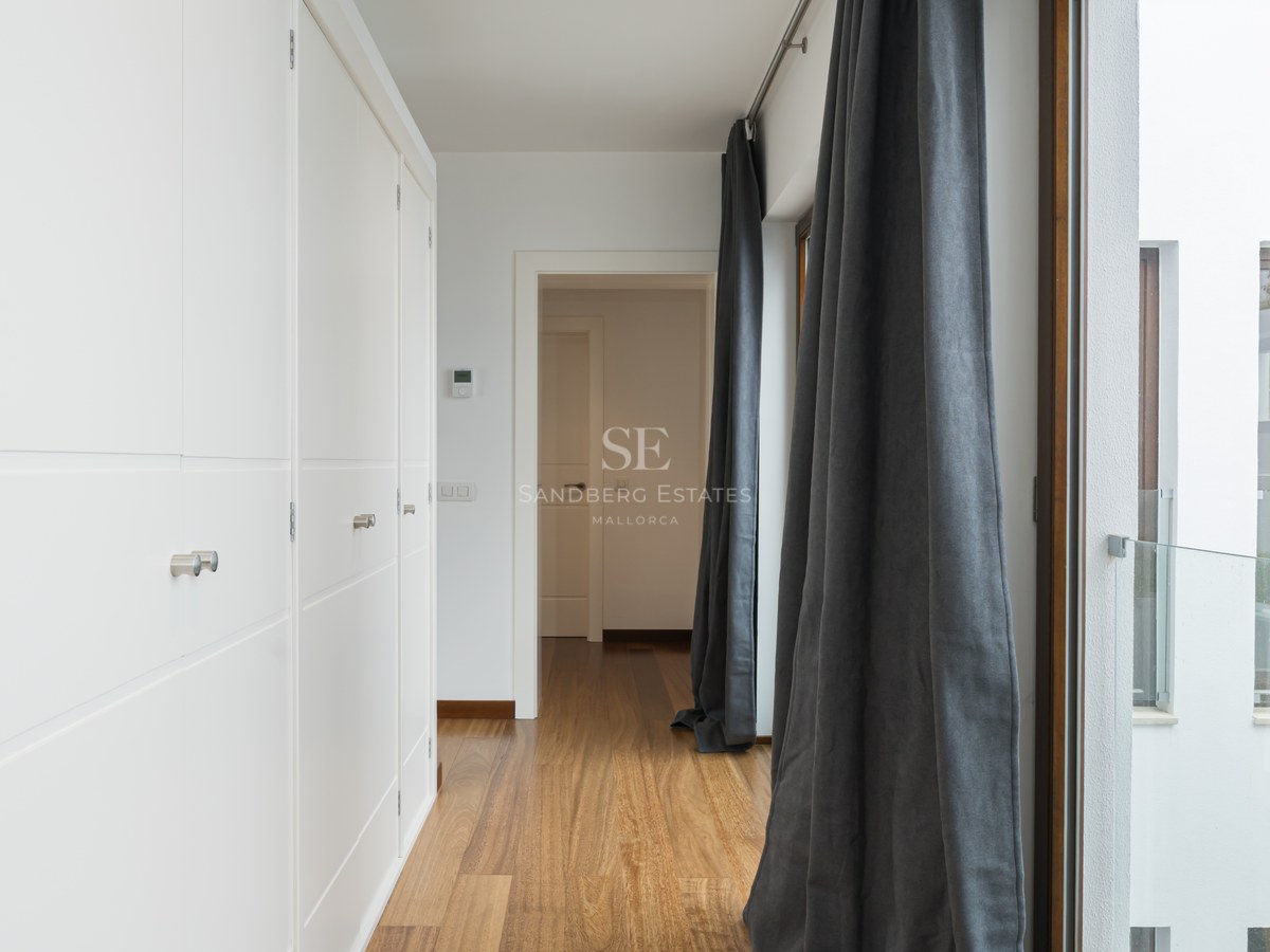 Pasillo luminoso con armarios empotrados blancos, suelos de madera cálida y cortinas de color gris marengo.