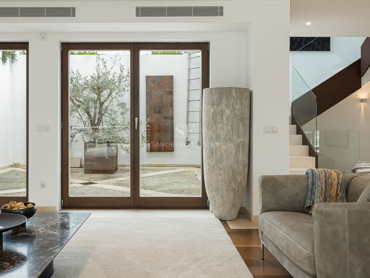 Salón moderno con sofá de cuero, mesa de mármol y grandes puertas de cristal que dan a un patio con un olivo.