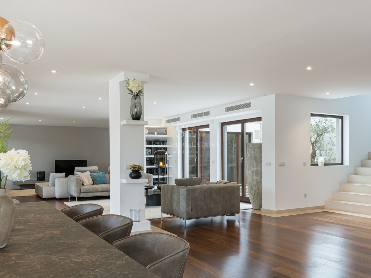 Amplio salón con suelos de madera oscura, mesa de piedra, lámpara de esferas de cristal y escalera de piedra natural.