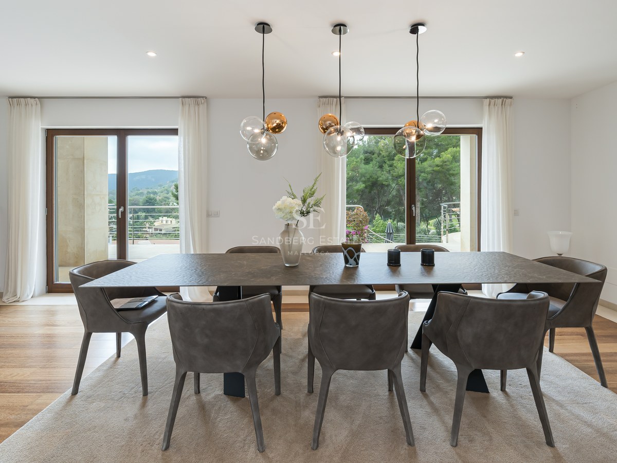 Zona de comedor moderna con mesa oscura texturizada, sillas grises, lámparas de diseño y grandes ventanales al exterior.