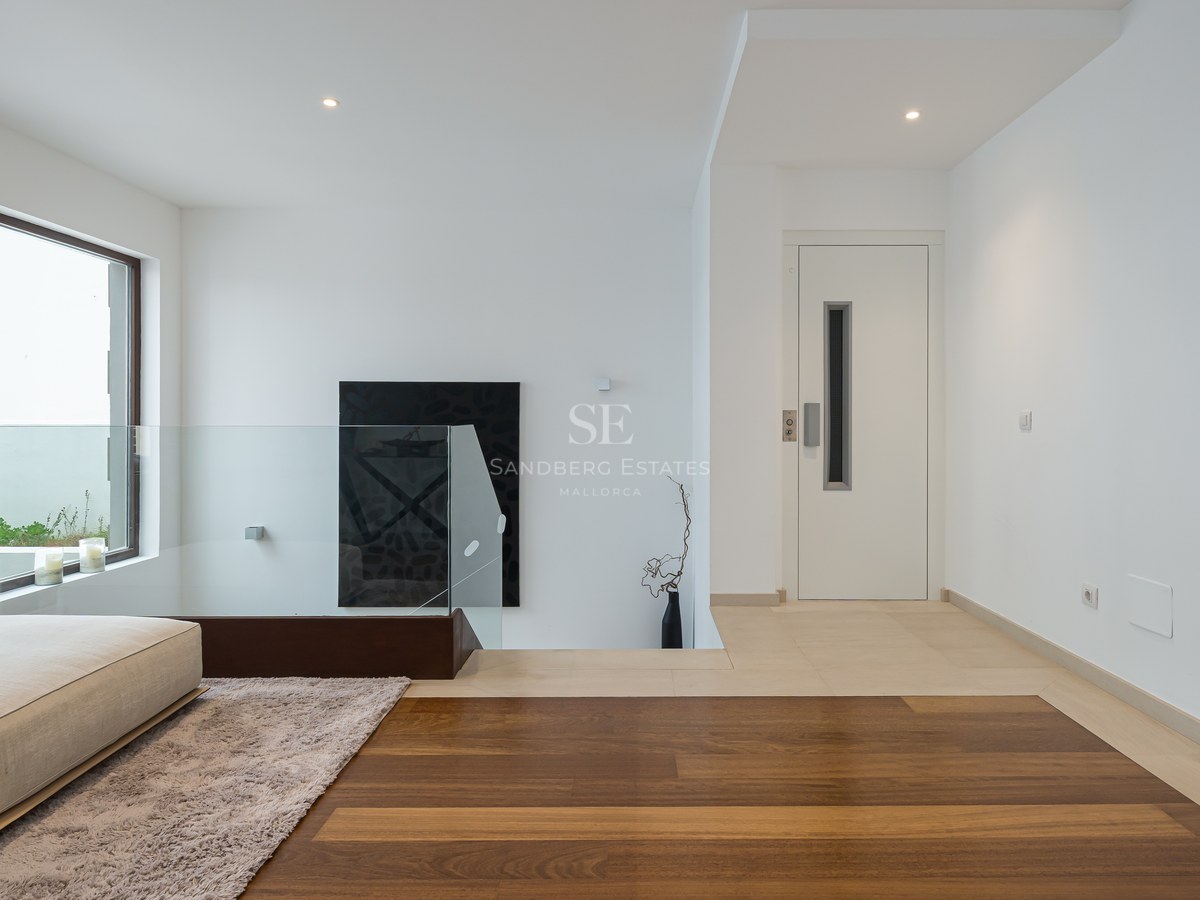 Distribuidor moderno con barandilla de cristal, suelo de madera de roble y puerta de ascensor blanca.
