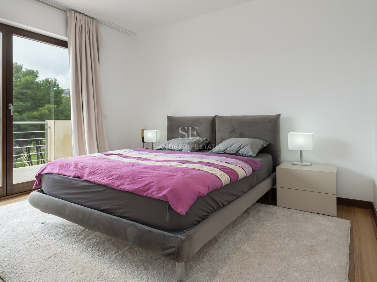 Dormitorio contemporáneo con cama tapizada gris, edredón púrpura, alfombra blanca y puerta de cristal a un balcón.