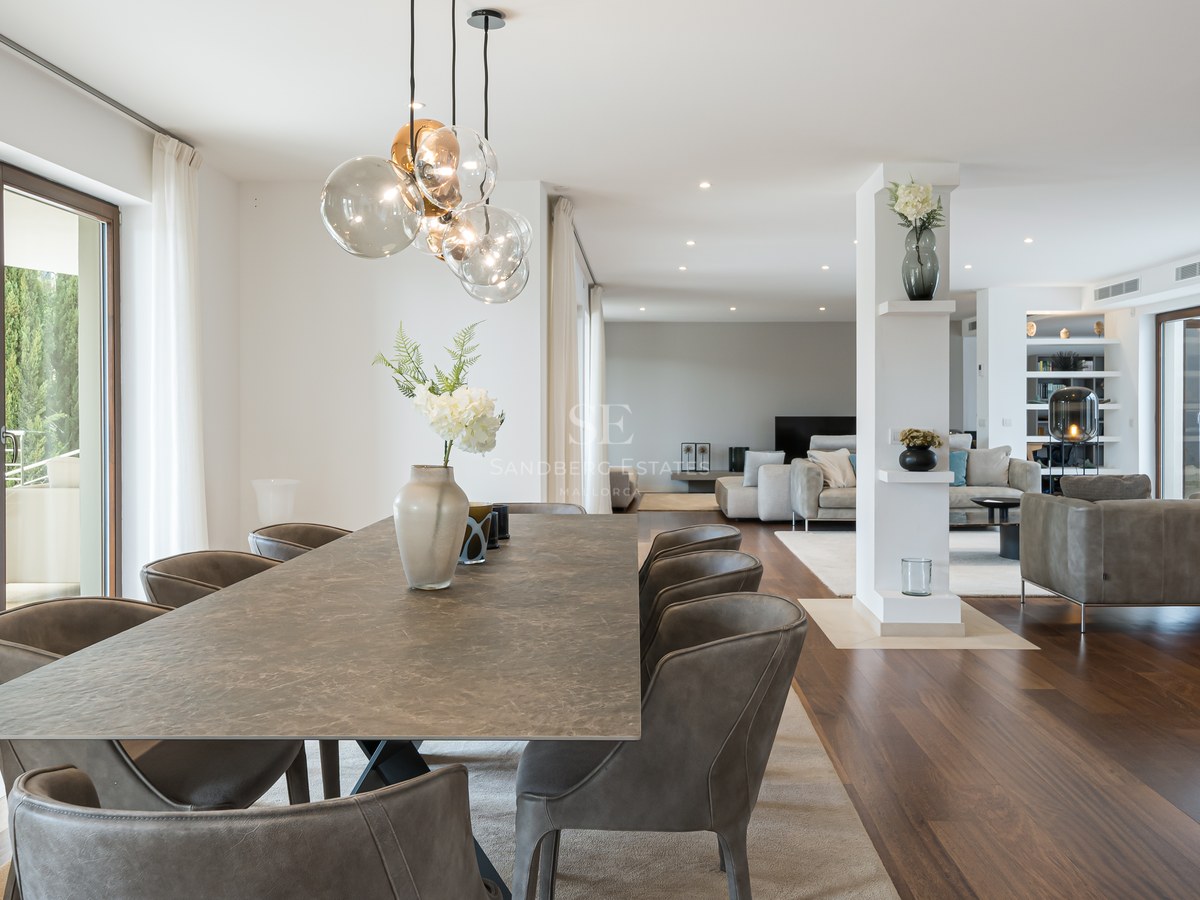 Mesa de comedor de piedra con sillas de cuero en una estancia luminosa con suelos de madera y puertas acristaladas.