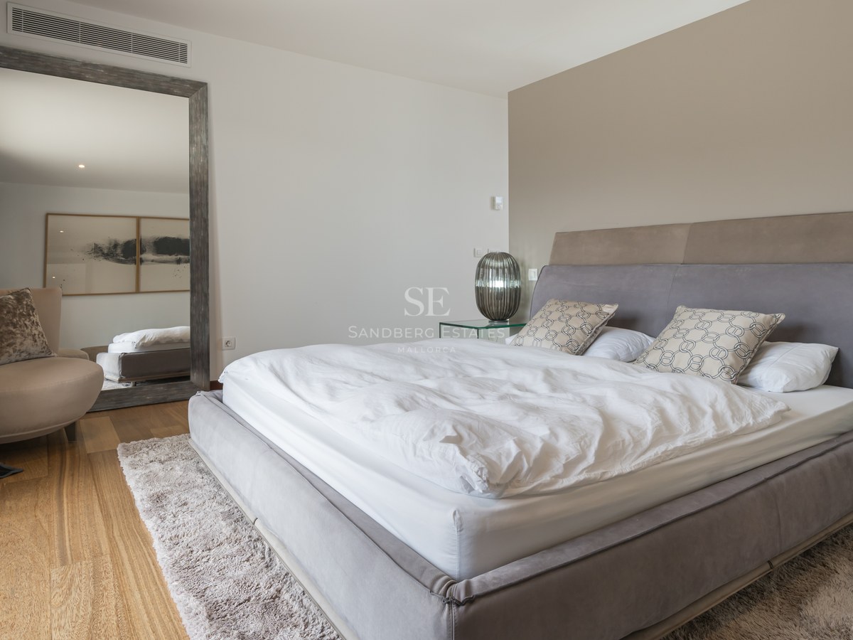 Dormitorio moderno con cama tapizada gris, suelo de roble, espejo de pie grande y mesitas de noche de cristal.