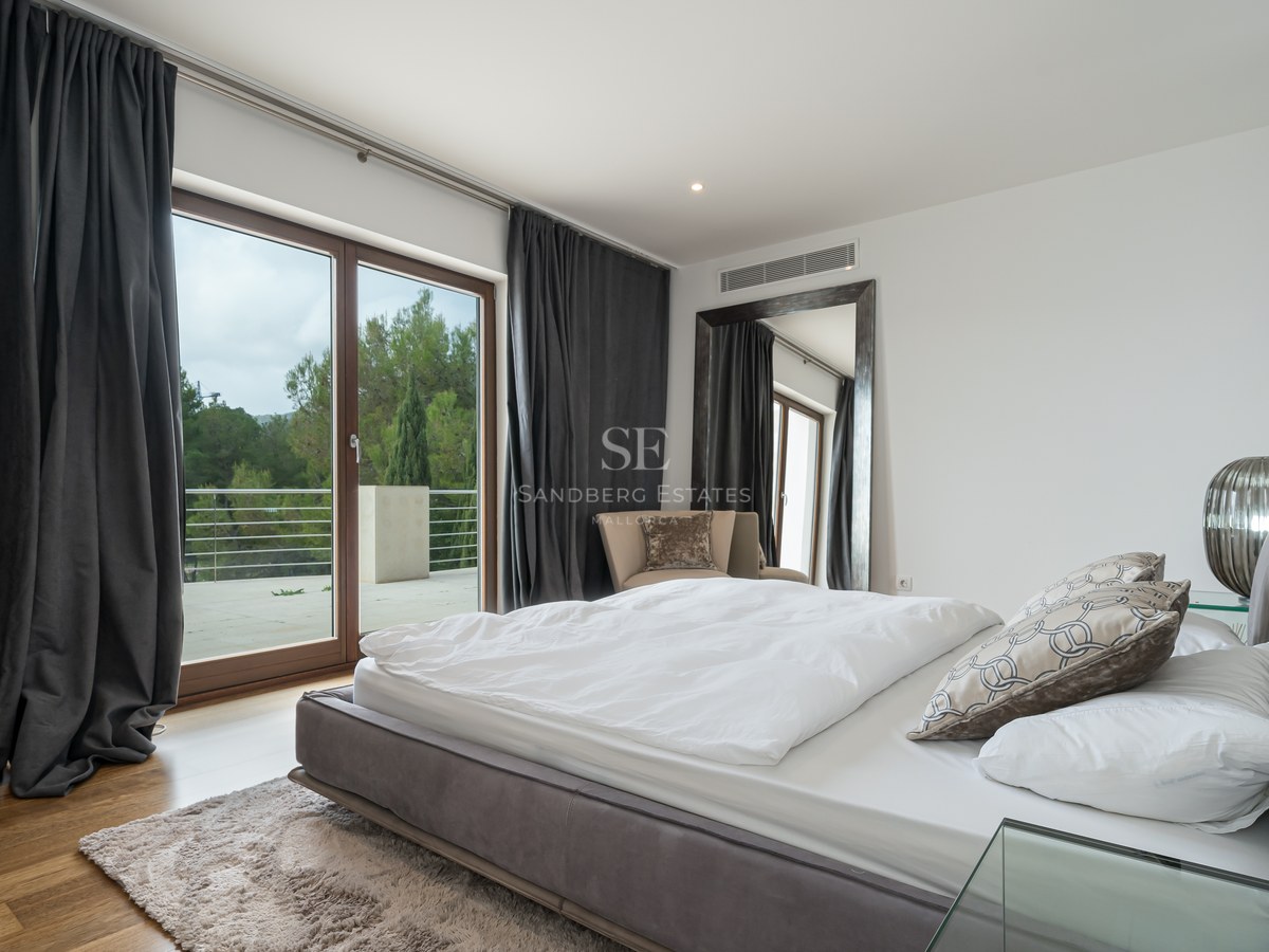 Dormitorio principal contemporáneo con cama blanca, cortinas antracita y puertas de cristal hacia una terraza con vistas.
