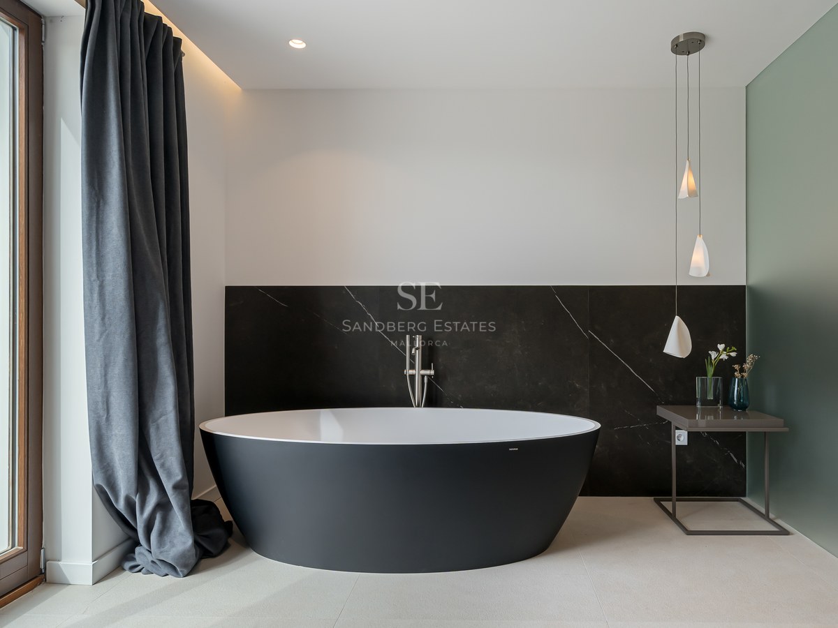 Baño principal moderno con bañera ovalada negra exenta frente a pared de mármol oscuro y luz natural.