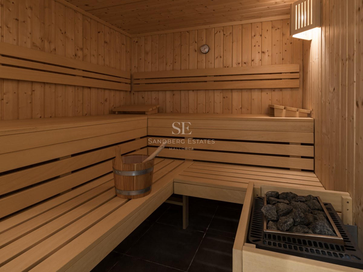 Vista interior de una sauna de madera con asientos a varios niveles, piedras térmicas y un cubo de madera.