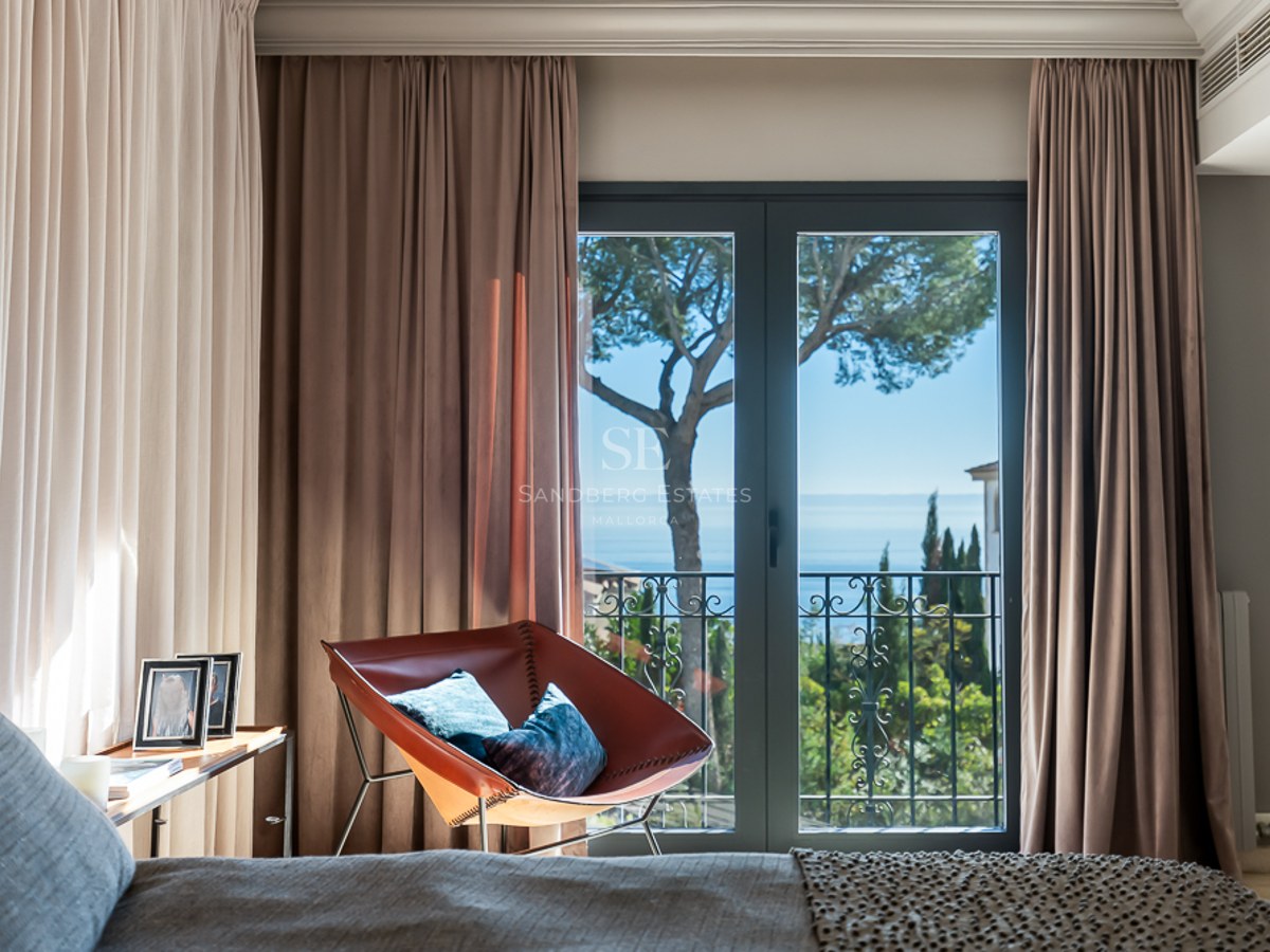 Dormitorio con sillón de cuero frente a ventanales con vistas al mar Mediterráneo y pinos.