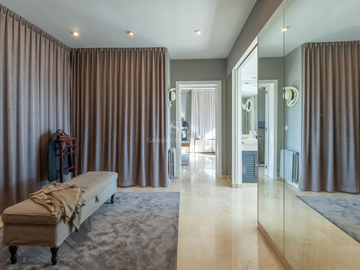 Vestidor moderno con suelos de mármol pulido, cortinas de suelo a techo, banco tapizado y grandes espejos.