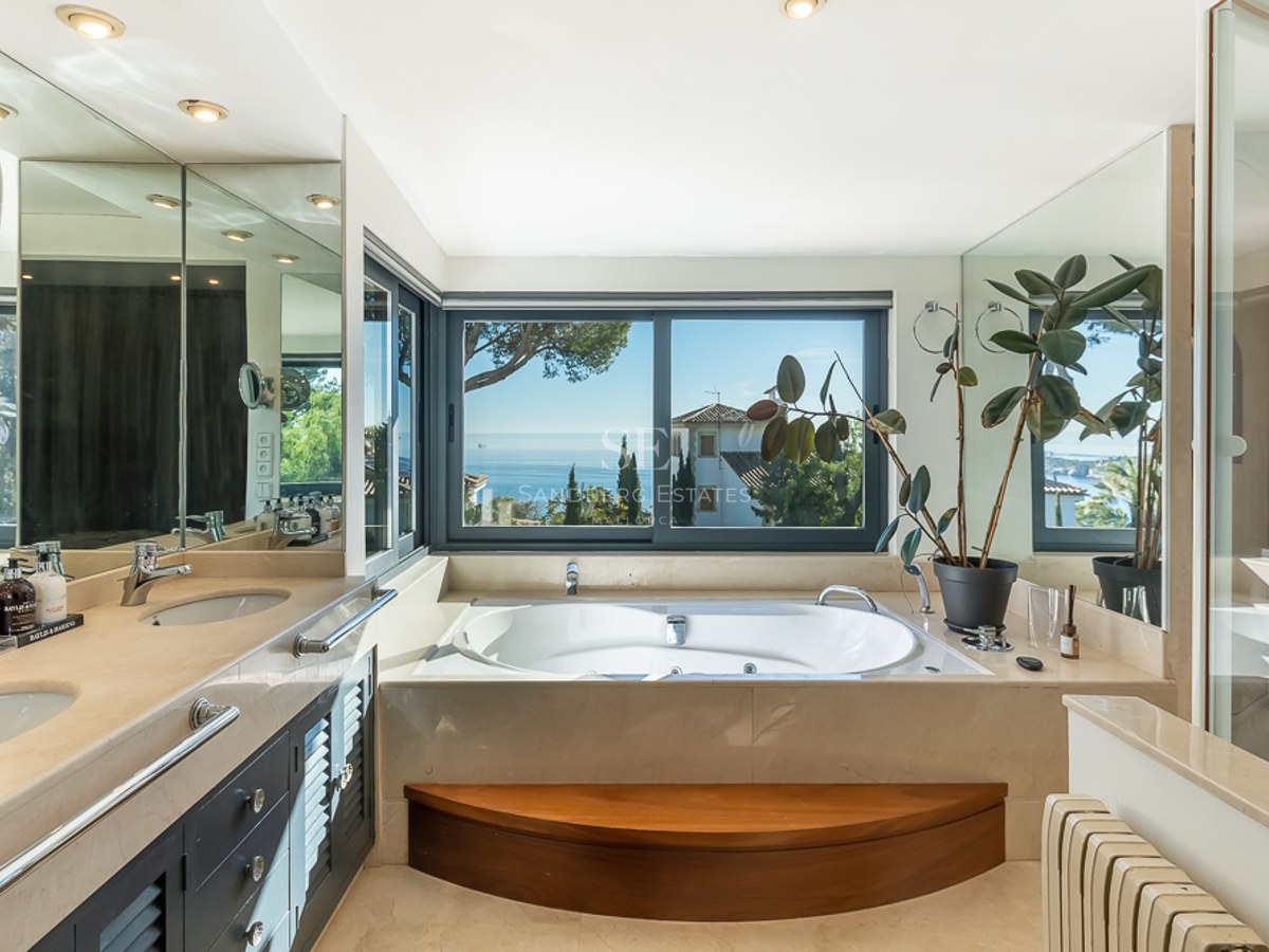 Baño de lujo con bañera de hidromasaje bajo una ventana con vistas panorámicas al mar Mediterráneo y tocador de mármol.
