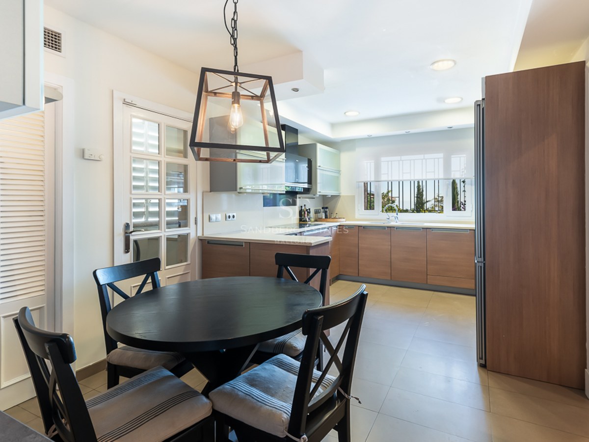 Cocina contemporánea con armarios de madera, encimeras blancas y mesa de comedor redonda negra con cuatro sillas.