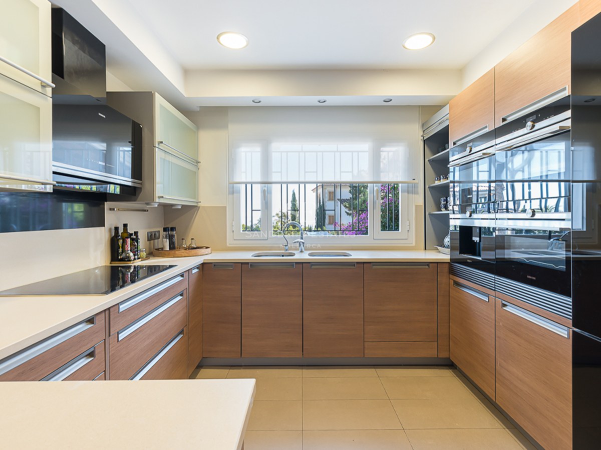 Cocina moderna con armarios de madera, encimeras blancas, electrodomésticos Siemens integrados y ventana al jardín.