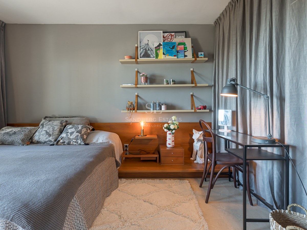 Dormitorio con ropa de cama gris, estanterías de madera integradas, escritorio de metal negro y cortinas grises.