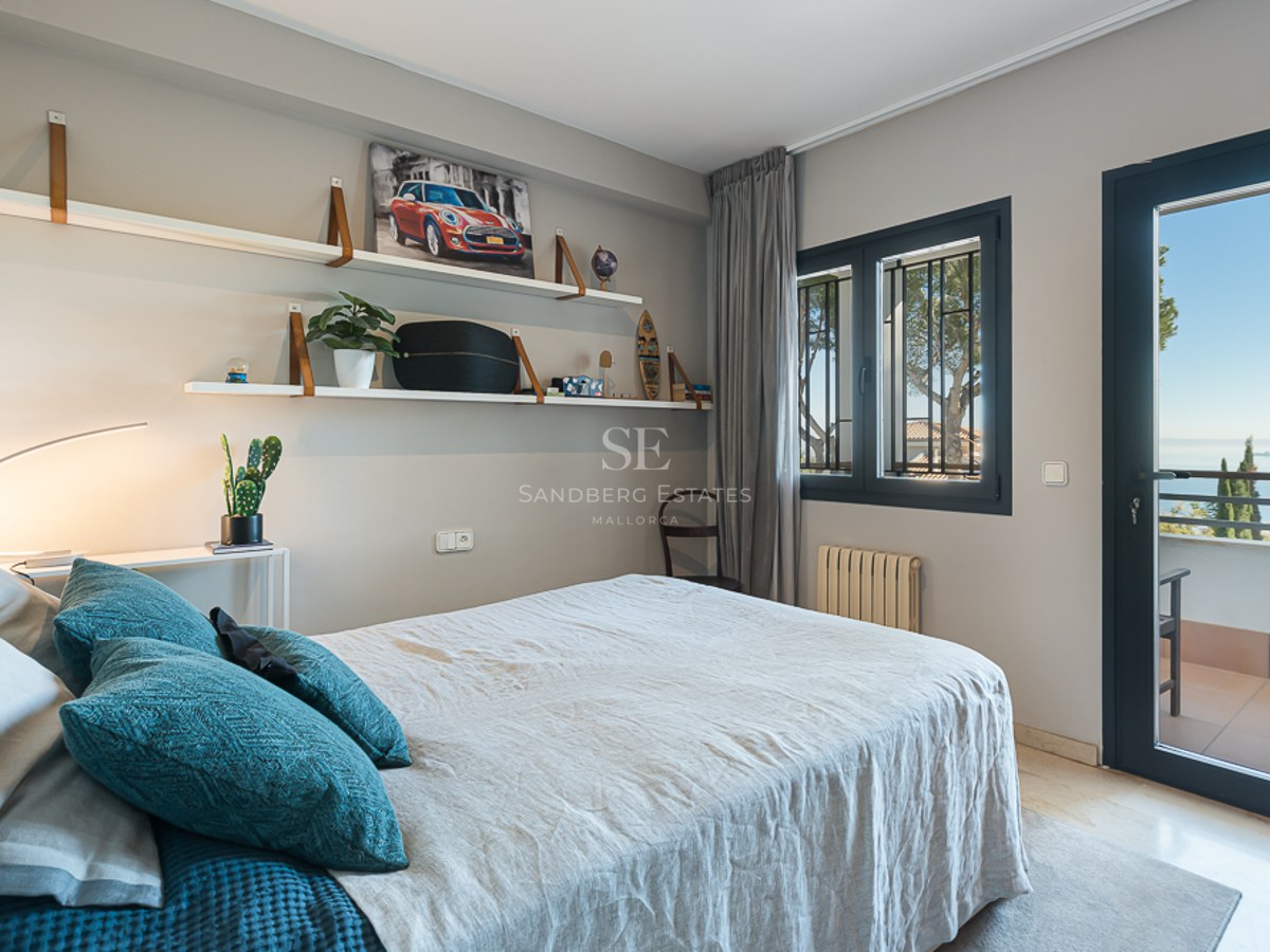 Dormitorio moderno con paredes grises, ropa de cama de lino, estanterías de diseño y puerta hacia un balcón con mar.