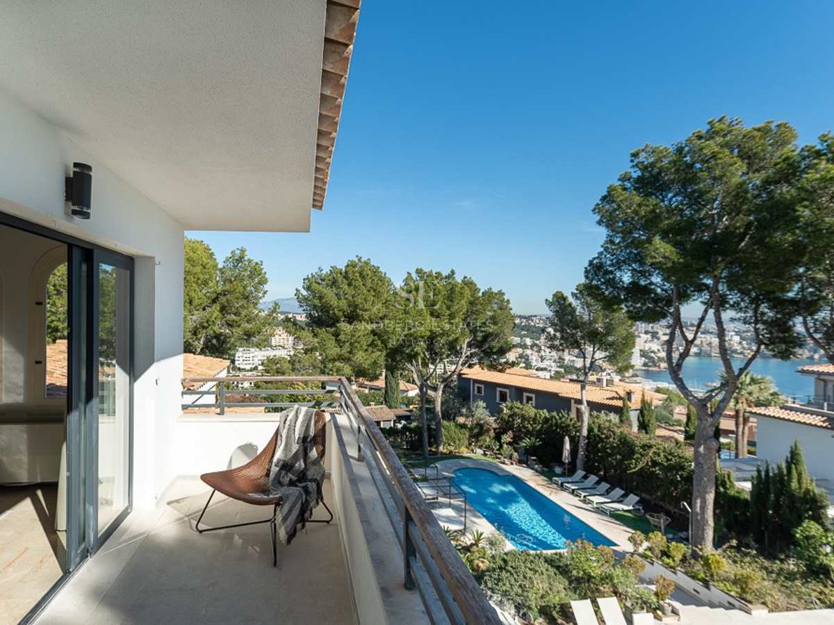 Balcón moderno con silla de diseño y vistas a una piscina, pinos y el mar Mediterráneo en Mallorca.