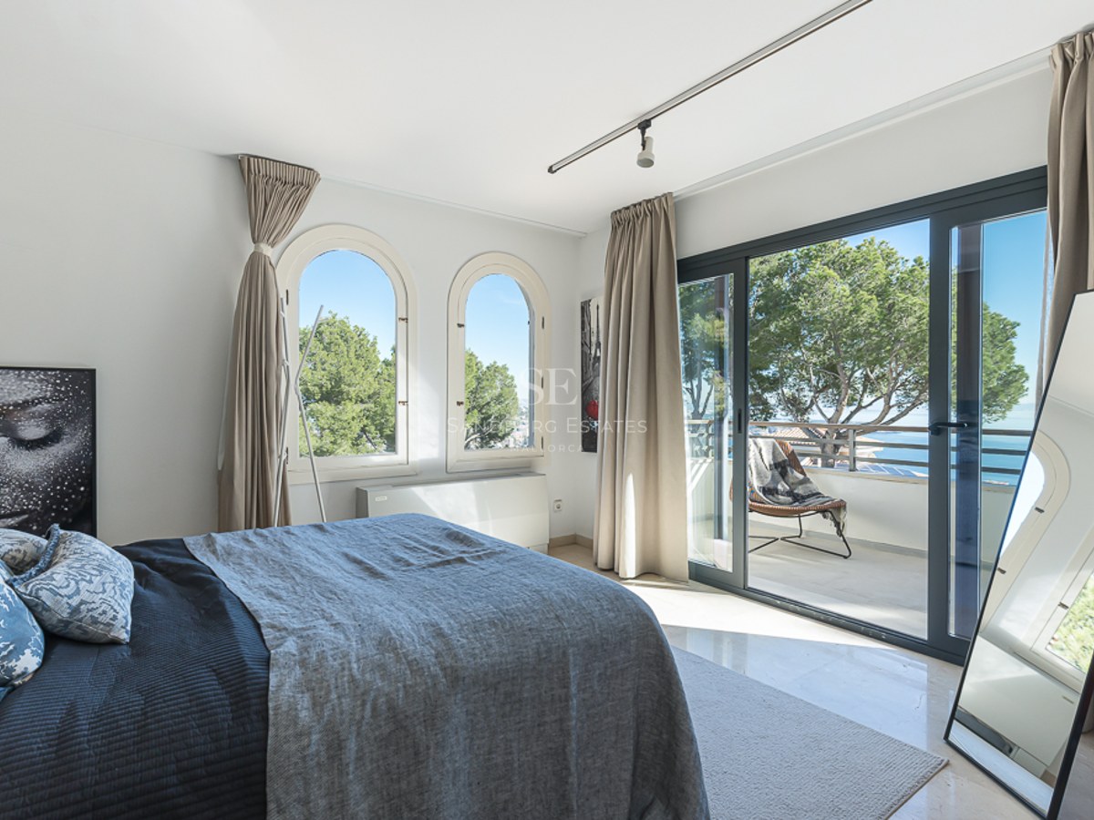 Dormitorio luminoso con ventanas en arco y acceso a terraza con vistas al Mediterráneo y pinos.