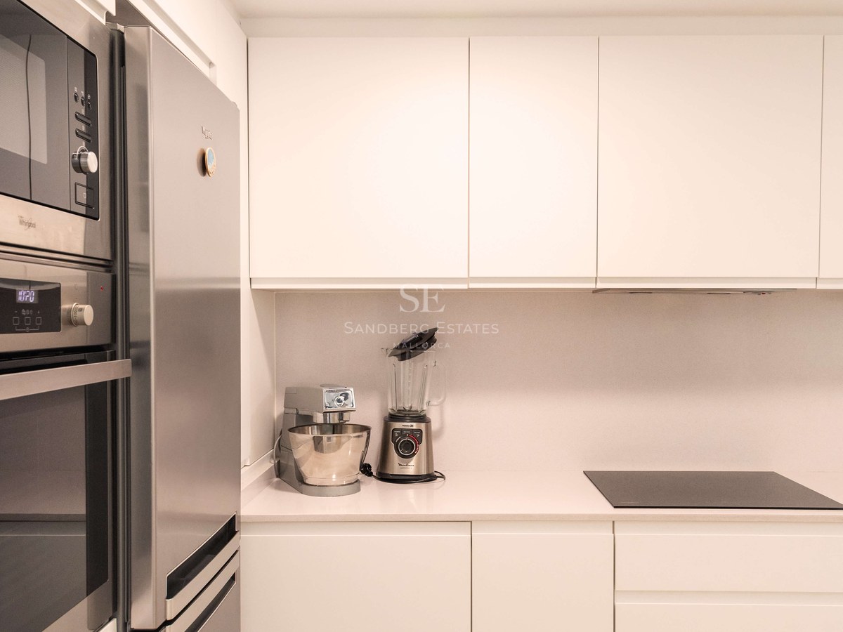 Cuisine blanche minimaliste, appareils en acier inoxydable, plan de travail en pierre et placards sans poignées.